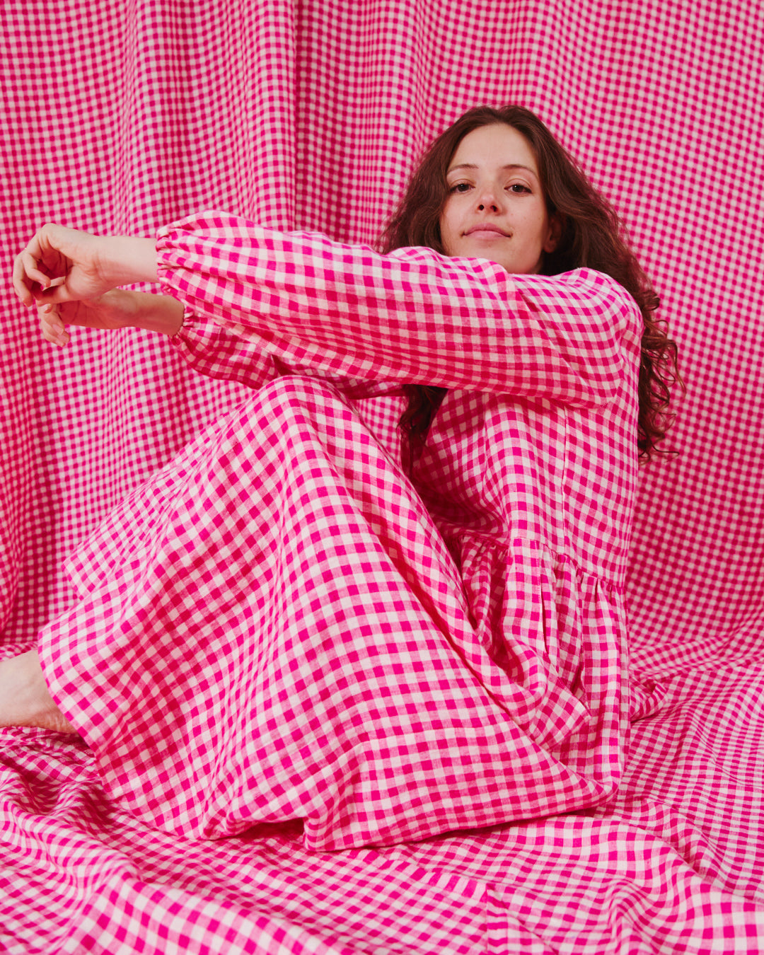 A person wearing a pink gingham linen dress sitting against a backdrop of pink gingham fabric.