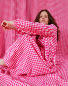 A person wearing a pink gingham linen dress sitting against a backdrop of pink gingham fabric.